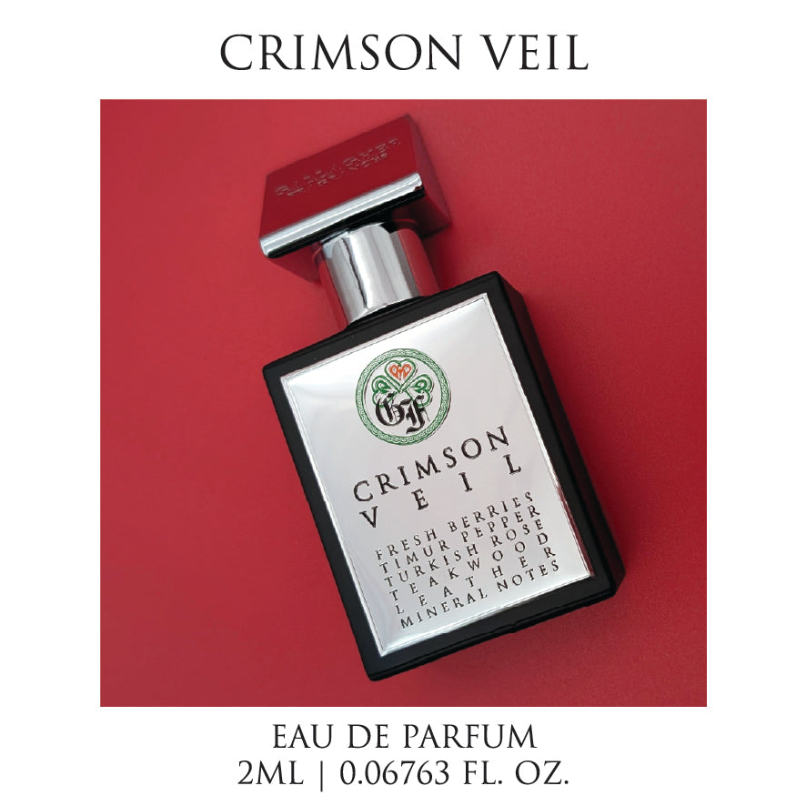 A bottle of Crimson Veil perfume with the label detailing the fragrance notes such as fresh berries, Turkish rose, teakwood, leather, and mineral notes, against a red background.