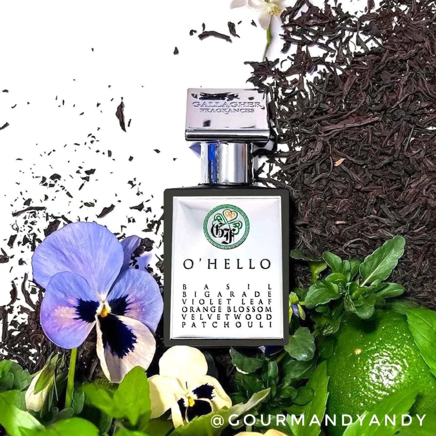 A bottle of 'O'Hello' perfume with a background of green leaves, black tea, and a purple flower.